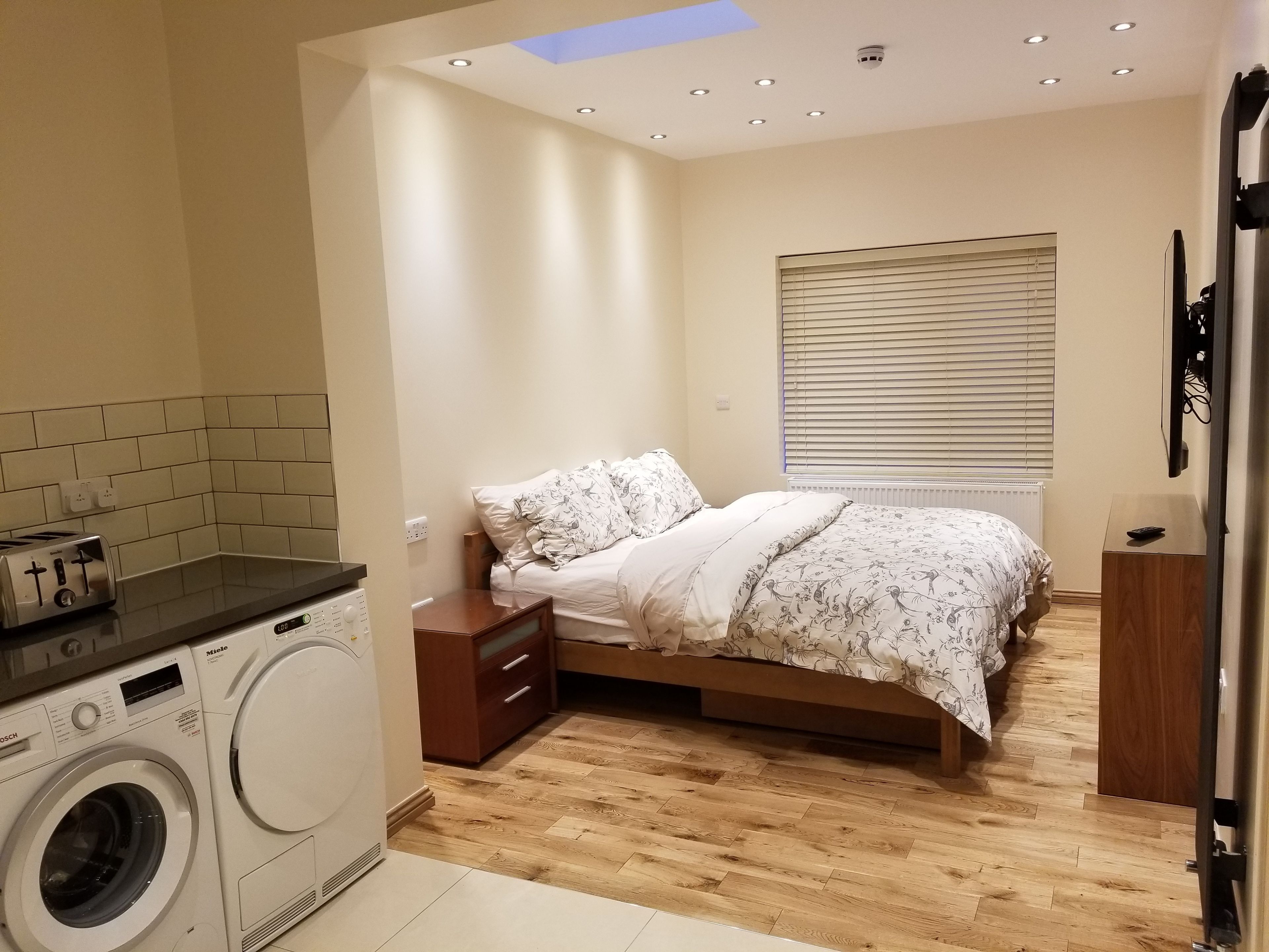 A compact bedroom with a bed, a nightstand, a dresser, and a washing machine.