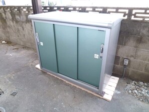Ein großer, grüner Verteilerkasten mit einer Metalttür, auf einer Betonfläche neben einer Ziegelwand platziert.