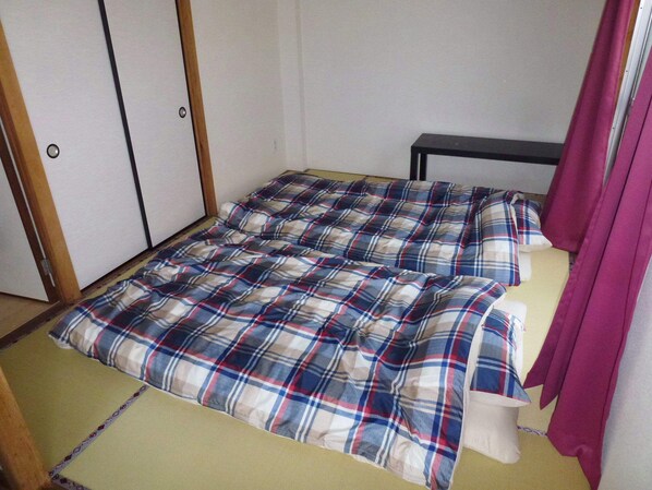 Ein kleines Zimmer mit einem Einzelbett, einer karierten Tagesdecke, einem Holzschrank und einem Vorhang.