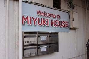 Ein Schild empfängt Besucher des Miyuki House, mit einer Metall-Klimaanlage und Briefschlitzen darunter.