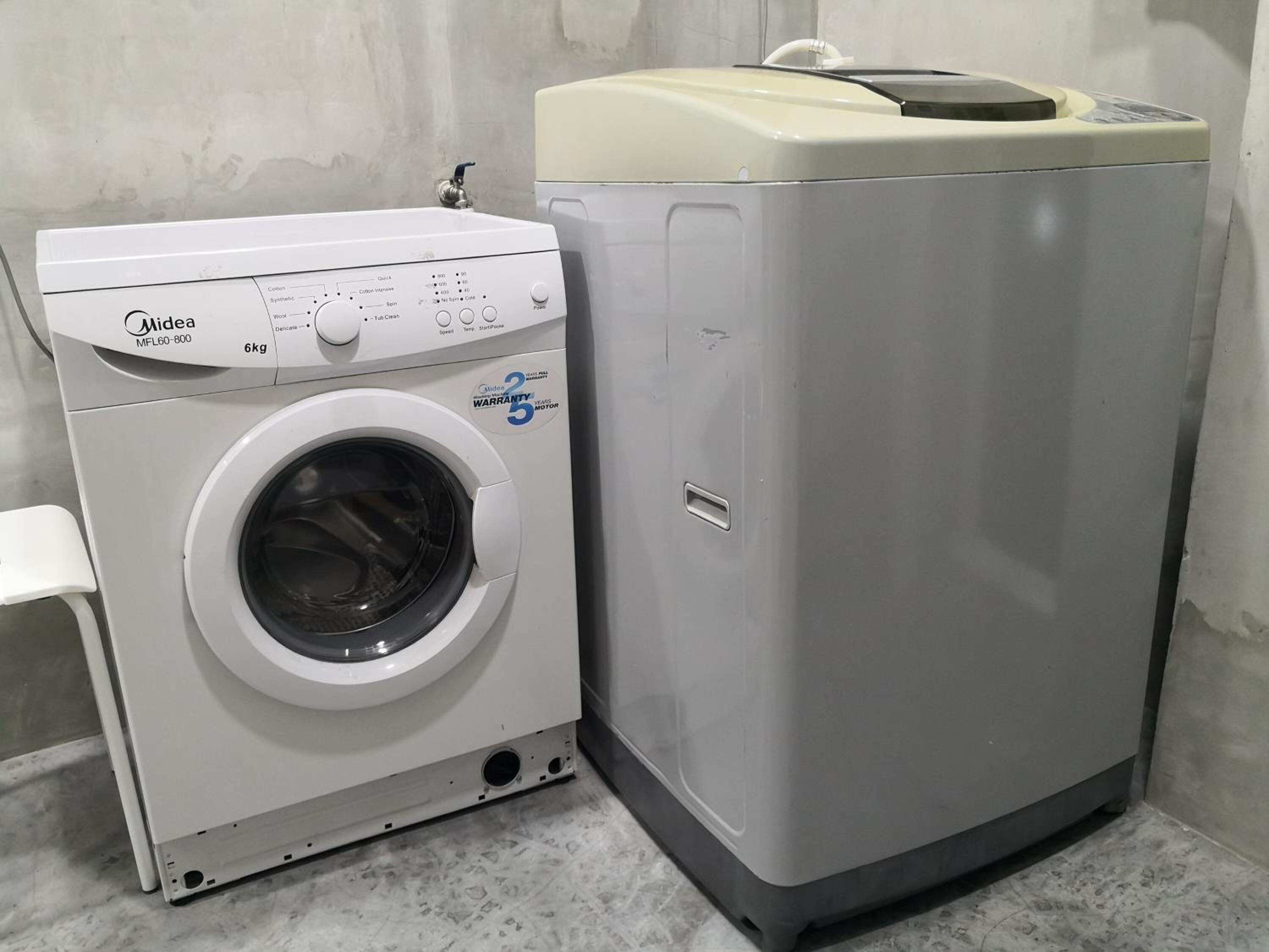 Een Midea wasmachine met voorlader en een droger met bovenlader, beide in een compacte, witte wasruimte met een betegelde vloer.