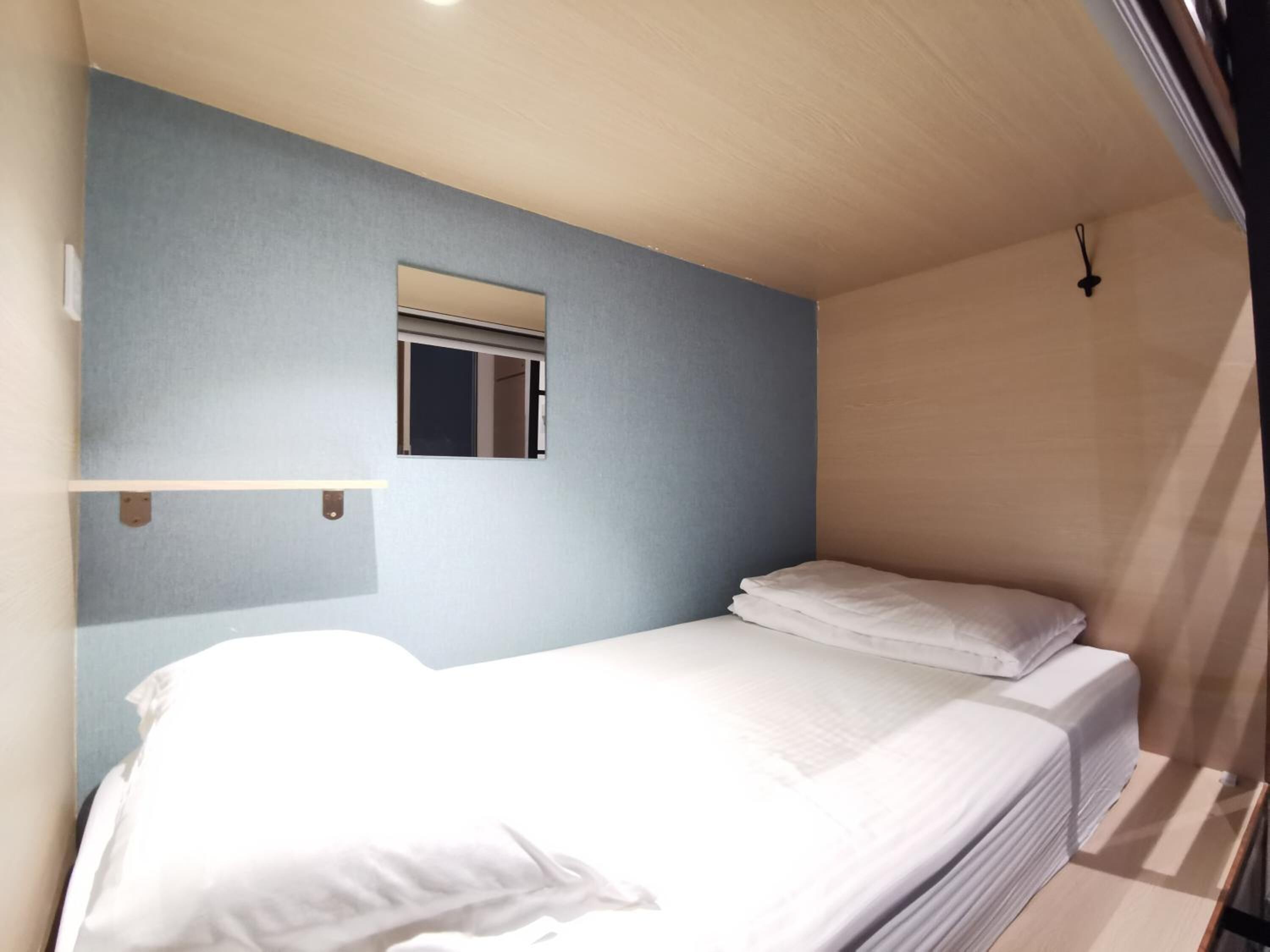 A small, single-bed room with a blue wall and a small window.