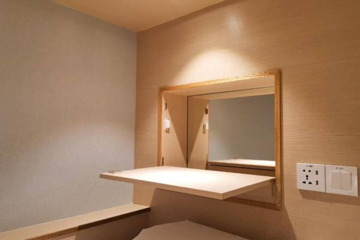 Une salle de bain avec un meuble-lavabo en bois, un miroir et un interrupteur.