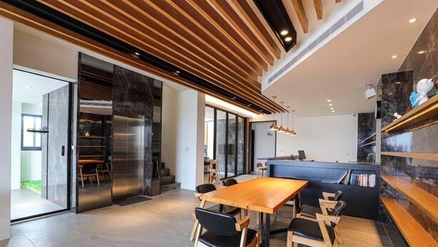 A modern kitchen with a wooden ceiling, a dining area with a wooden table and chairs, and a built-in bookshelf.