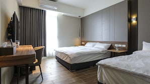 A hotel room with two beds, a desk, a chair, and a large window with curtains.