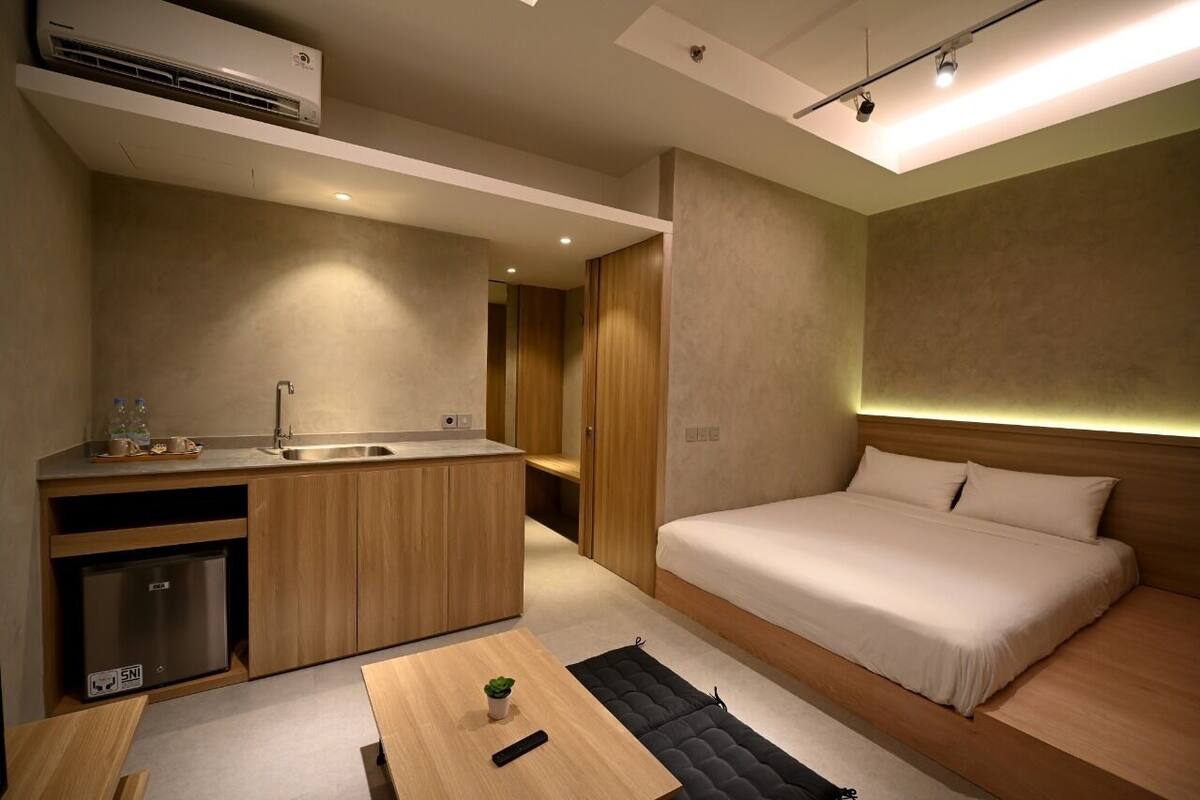 A compact hotel room with a kitchenette, a bed, and a small table with a plant.