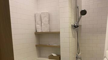 Un baño pequeño con azulejos blancos, que incluye un inodoro, ducha y un estante con toallas.