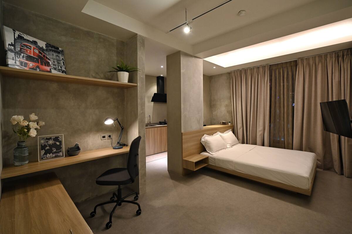 A modern bedroom with a bed, desk, chair, and a TV.