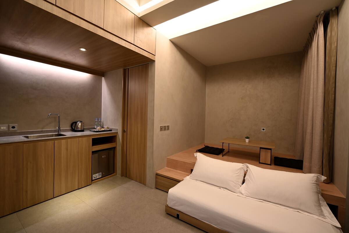 A compact bedroom with a bed, a small desk, and a kitchenette.