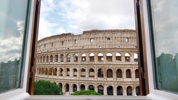 A view of the Colosseum through a window, featuring its ancient architecture and multiple arches. - Magia at Colosseum (Rome)