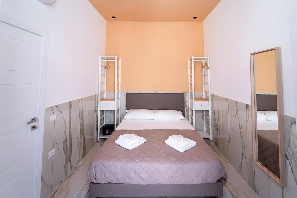Une chambre d’hôtel comprenant un lit, deux tables de chevet, une armoire, un miroir et des murs décorés d’un motif imitant le marbre.