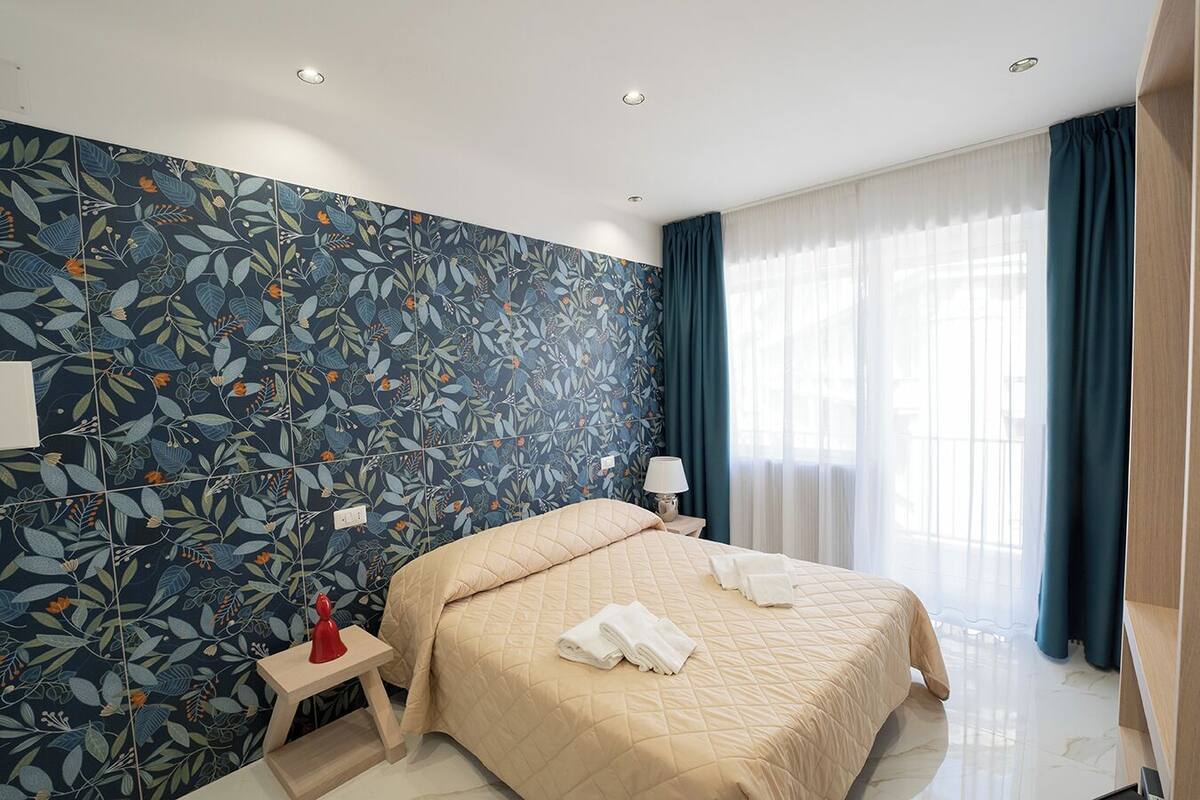 Une chambre d’hôtel avec un grand lit, une table de chevet, une lampe et une fenêtre avec des rideaux.