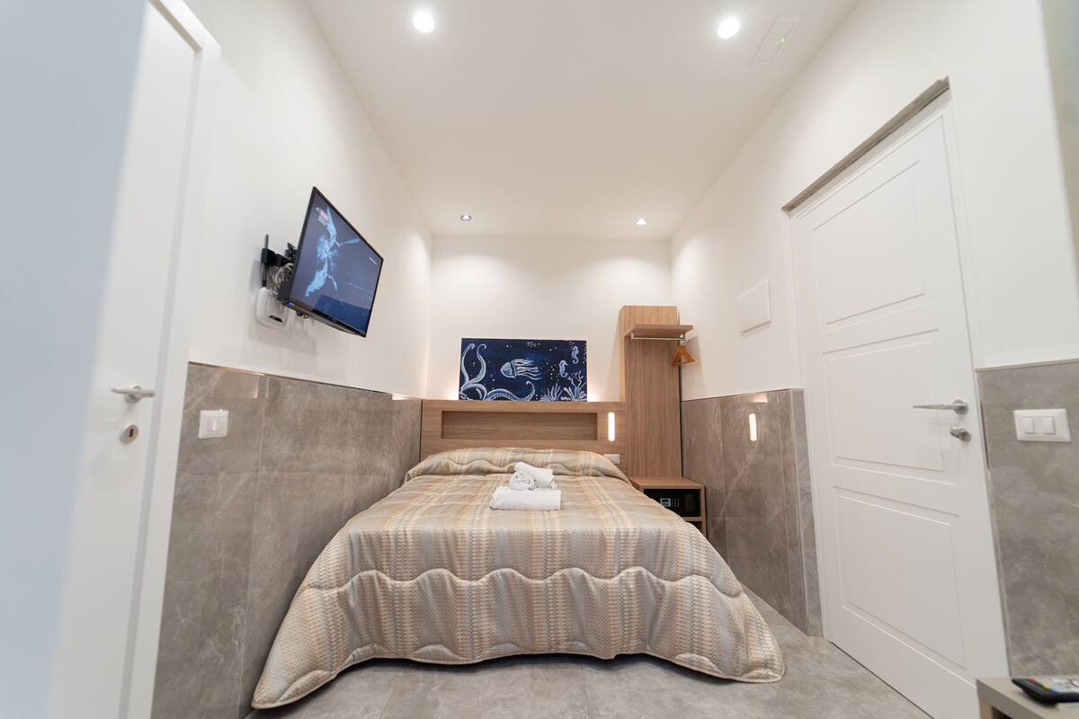 Une chambre d’hôtel moderne dotée d’un grand lit, d’un téléviseur à écran plat fixé au mur et d’une tête de lit en bois.