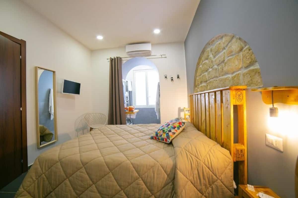 Une chambre à coucher avec un grand lit, une tête de lit en bois, un miroir, une télévision et une arche en pierre.