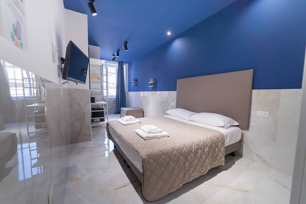 Une chambre moderne avec un grand lit, un téléviseur fixé au mur et une salle de bain équipée d’une douche et de toilettes.