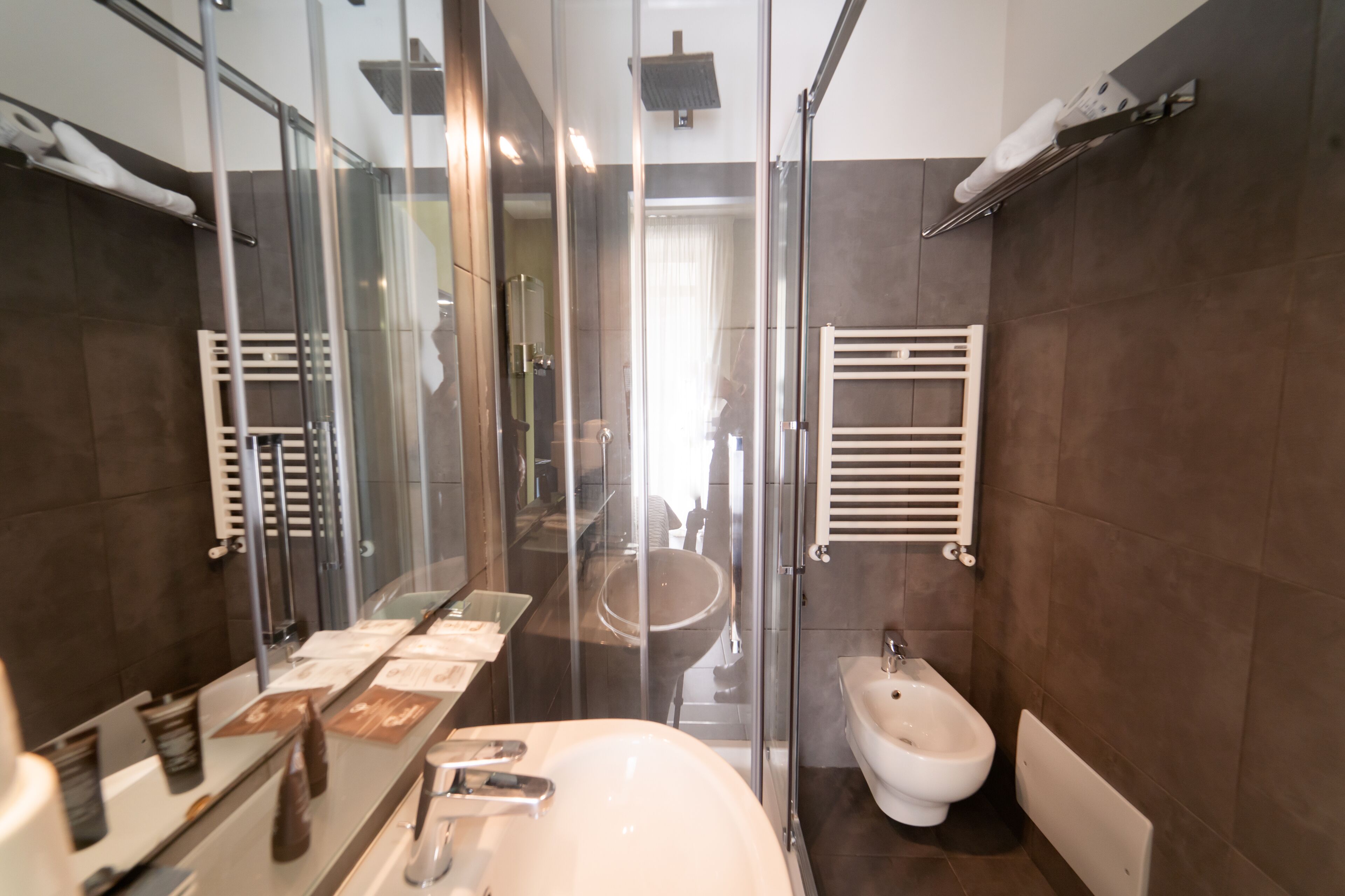 A modern bathroom with a glass shower enclosure, a large mirror, a white sink, and a bidet.