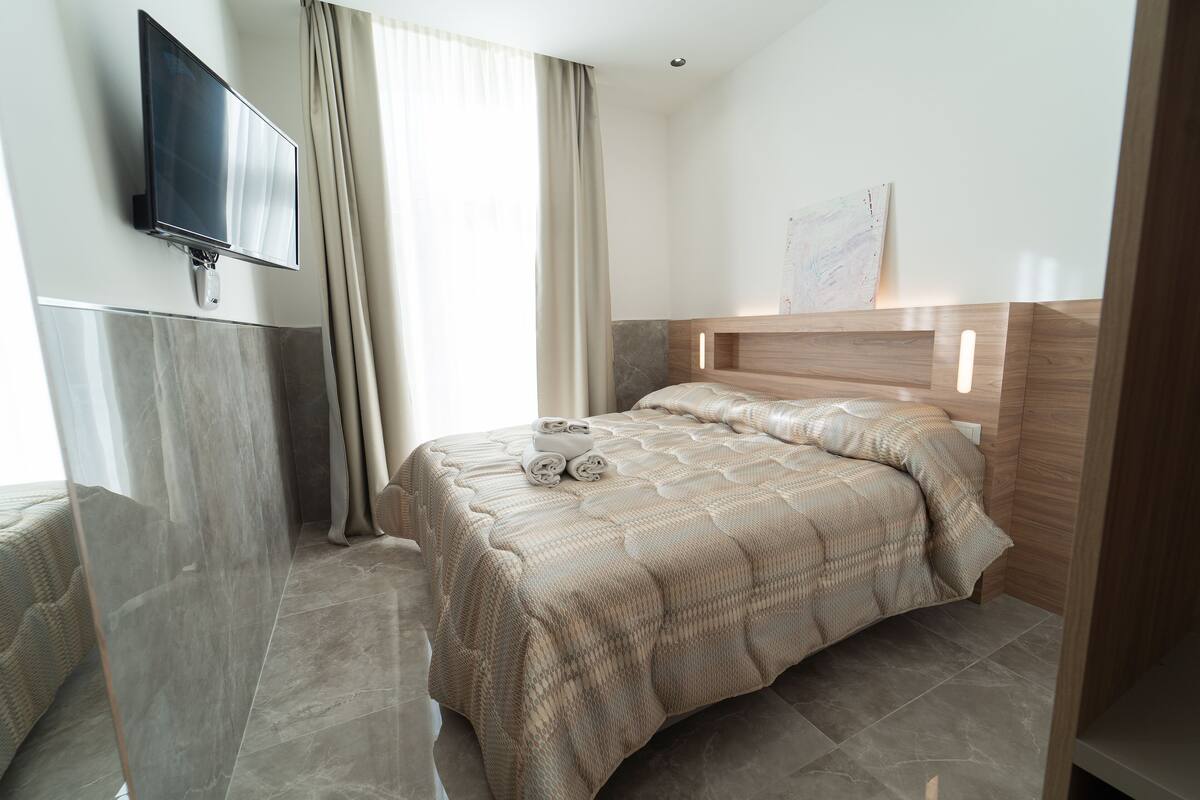 Une chambre d’hôtel moderne dotée d’un grand lit, d’un téléviseur à écran plat fixé au mur et d’une grande fenêtre avec des rideaux.