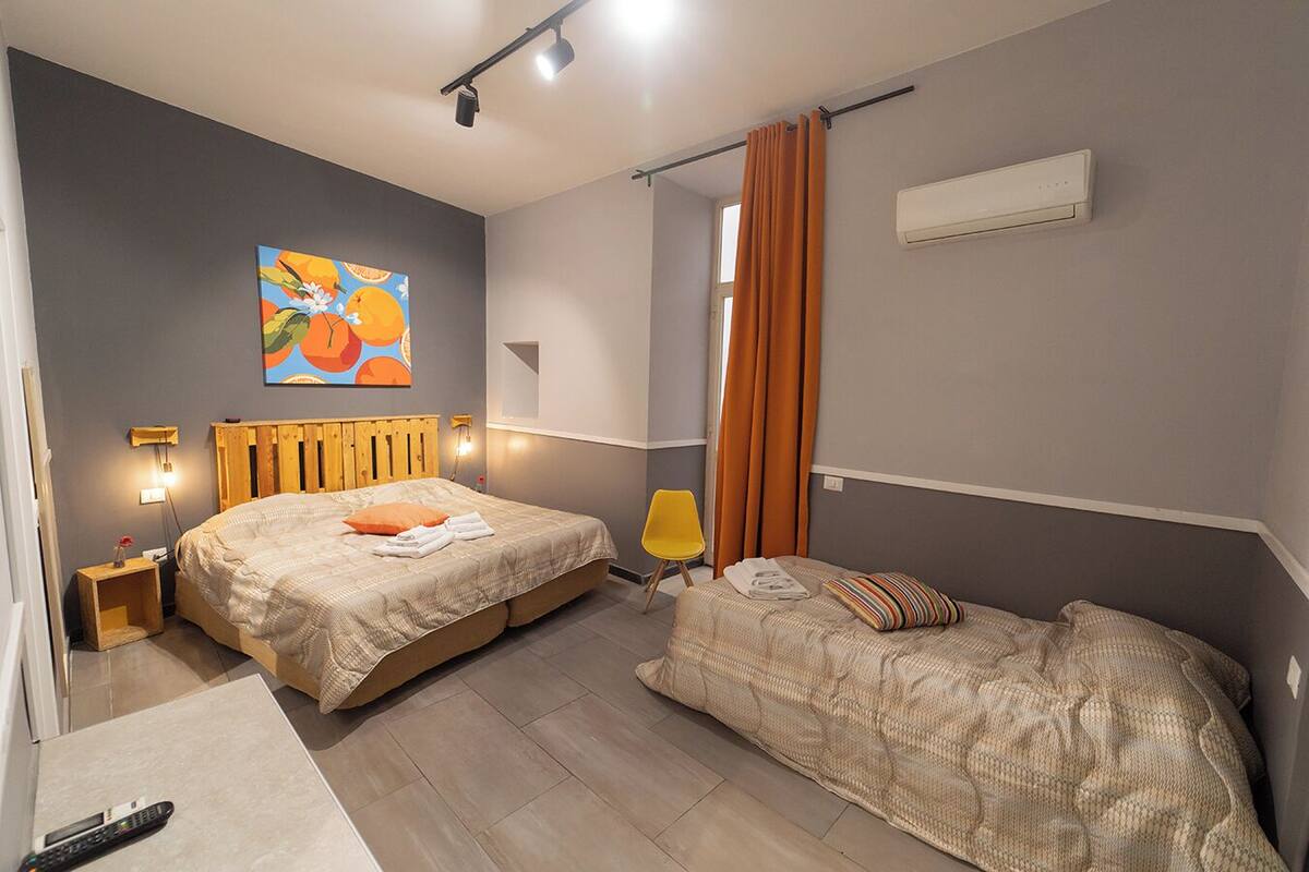 Une chambre avec deux lits, un tableau, une table de chevet, une lampe et un appareil de climatisation.