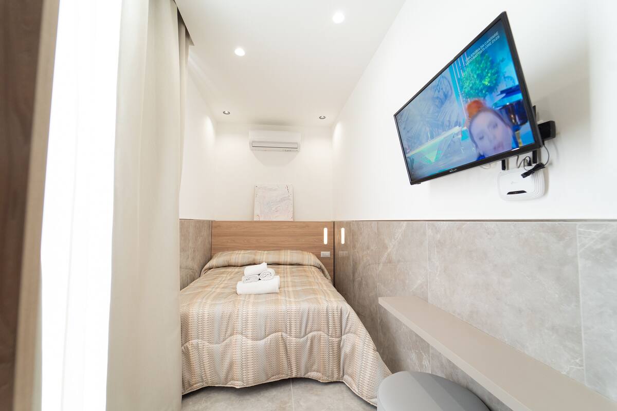 Une chambre d’hôtel moderne équipée d’un lit, d’un téléviseur fixé au mur et d’une banquette intégrée.