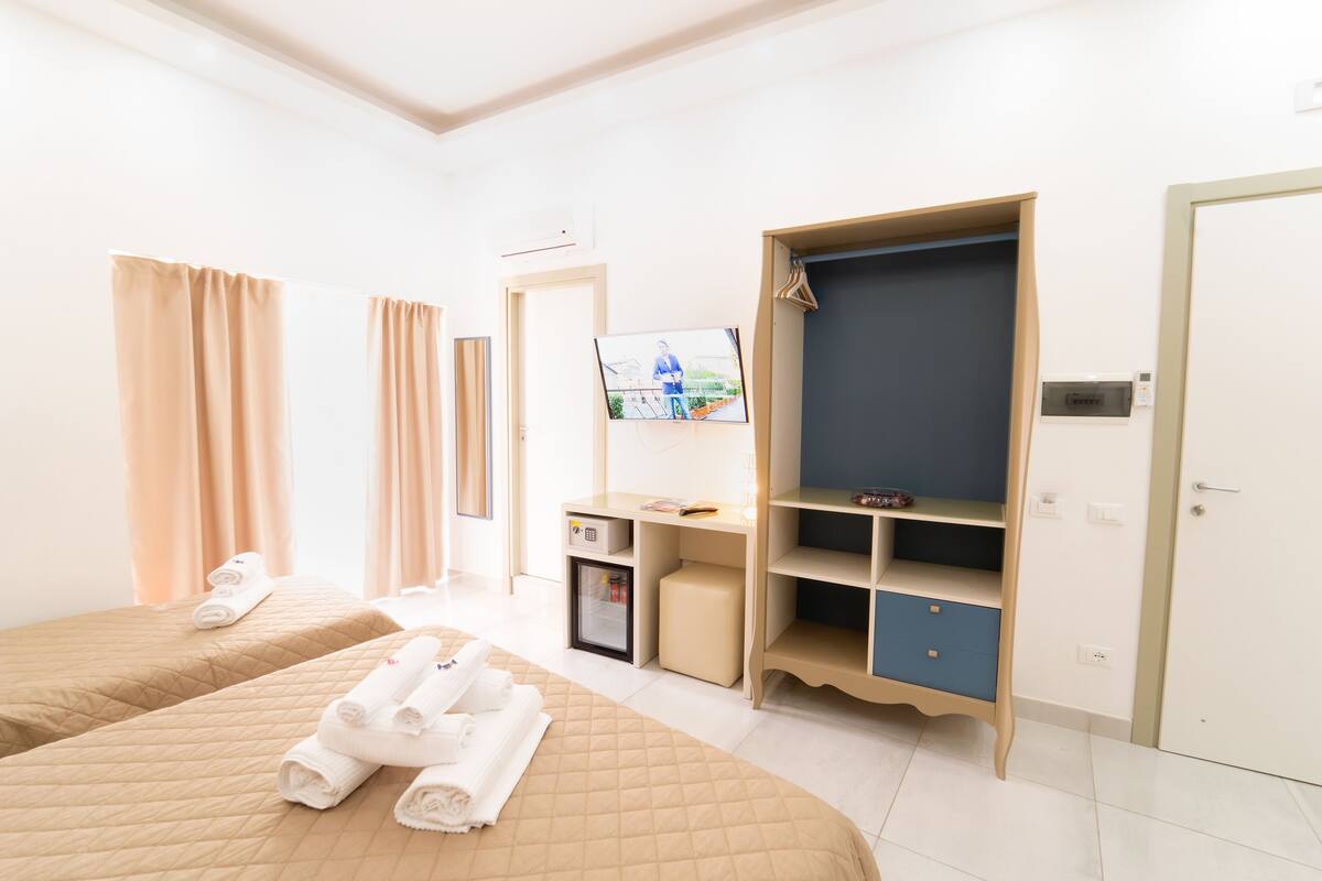 Une chambre d’hôtel avec deux lits, une armoire, un bureau, une télévision et un petit réfrigérateur.