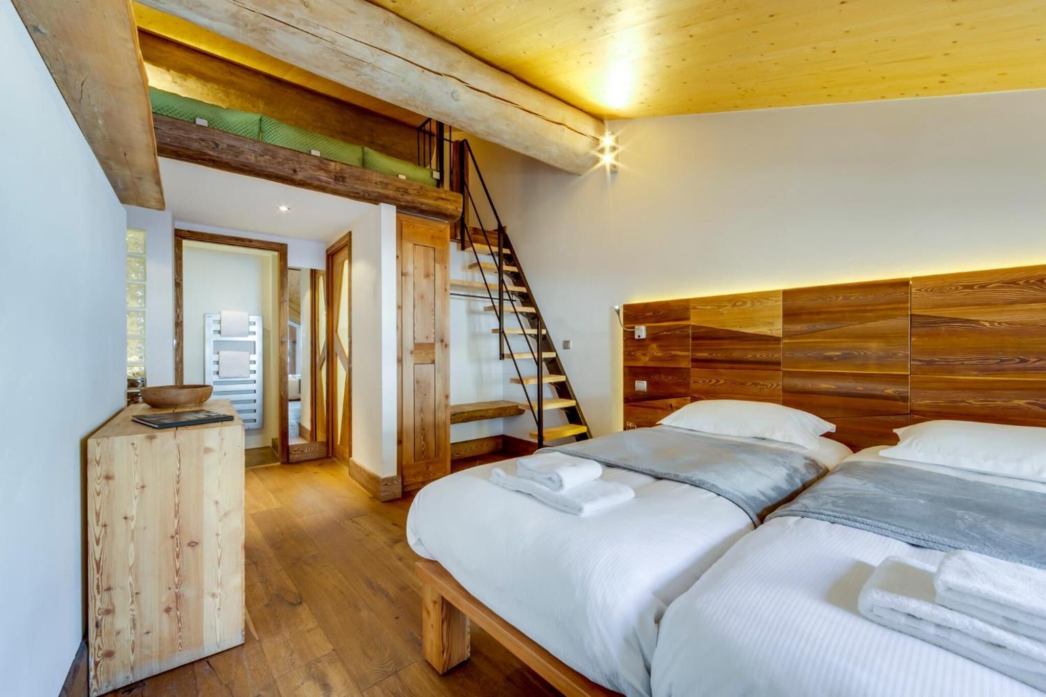 A bedroom with a wooden headboard, a bed with white linens, a wooden nightstand, and a staircase leading to an upper level.