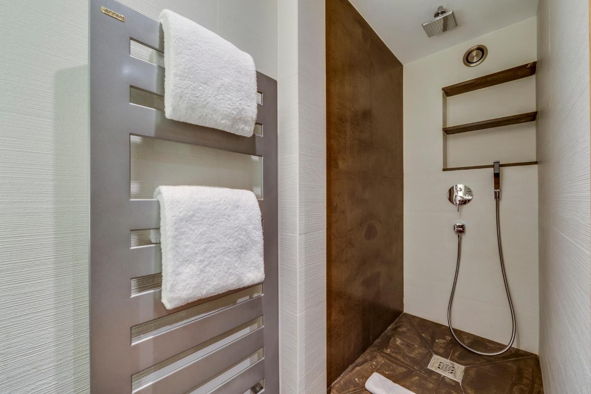 Ein Badezimmer mit Handtuchhalter, zwei weißen Handtüchern, einer Duschkabine mit Duschbrause und einer Wand mit Holzelementen.