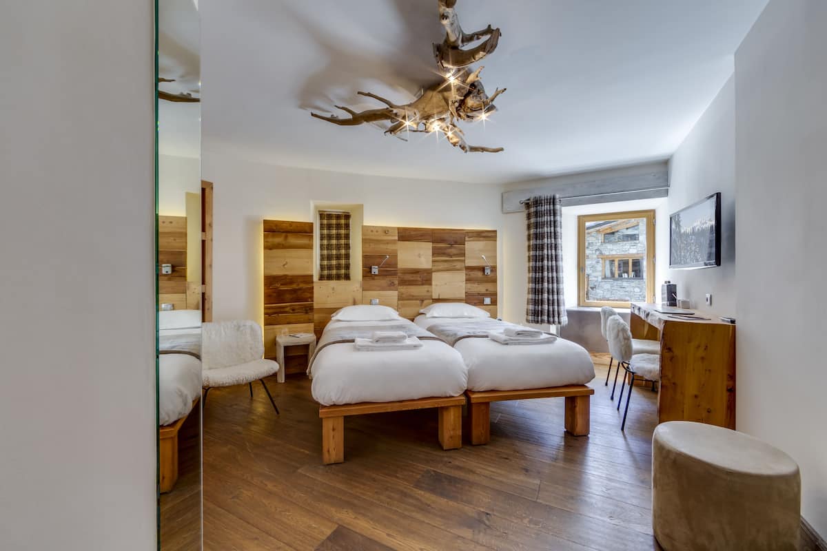 Una habitación de hotel moderna con suelo de madera, dos camas, un escritorio y un ventanal grande.