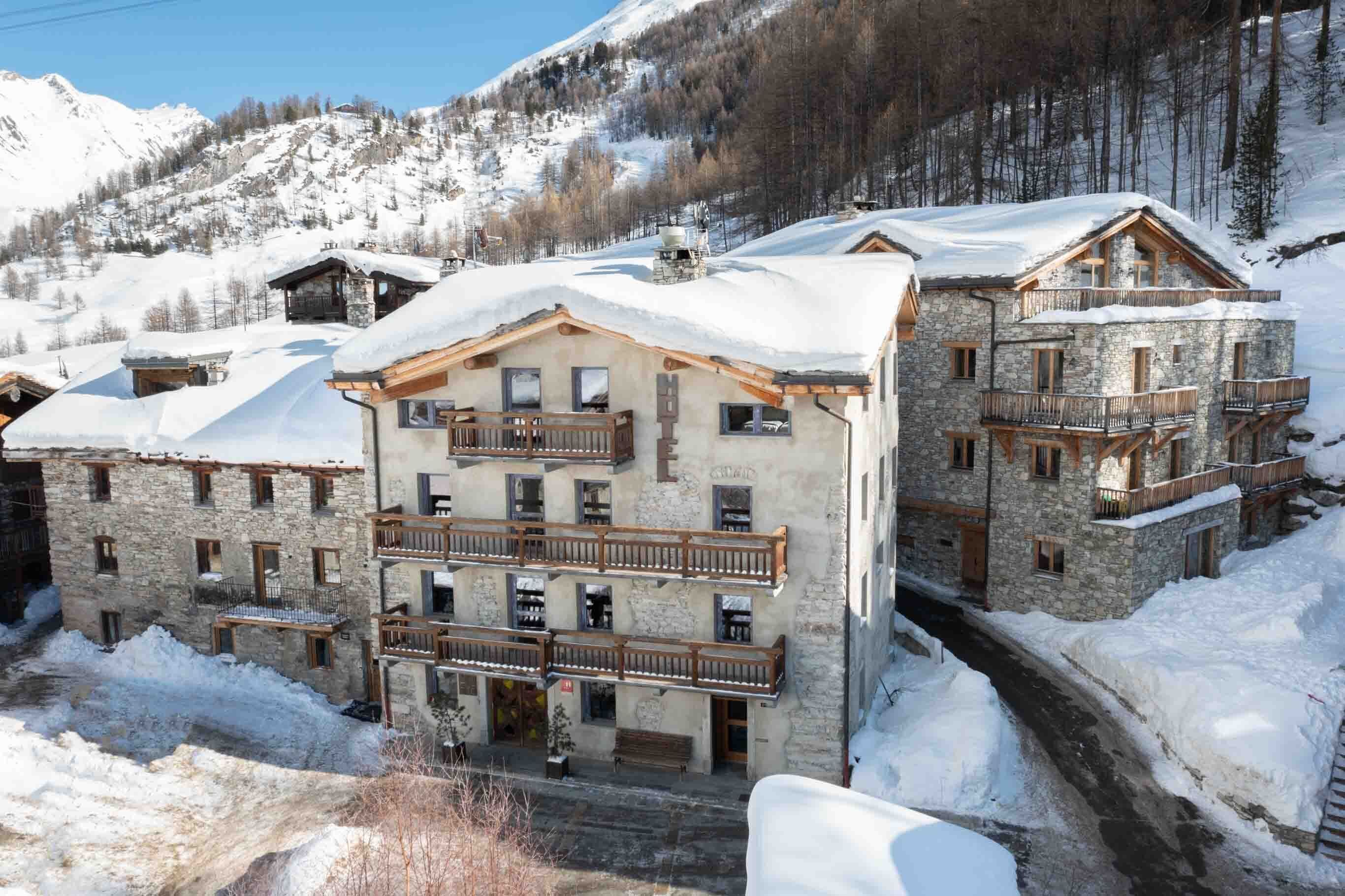 A multi-story stone building with balconies, surrounded by snow-covered mountains.