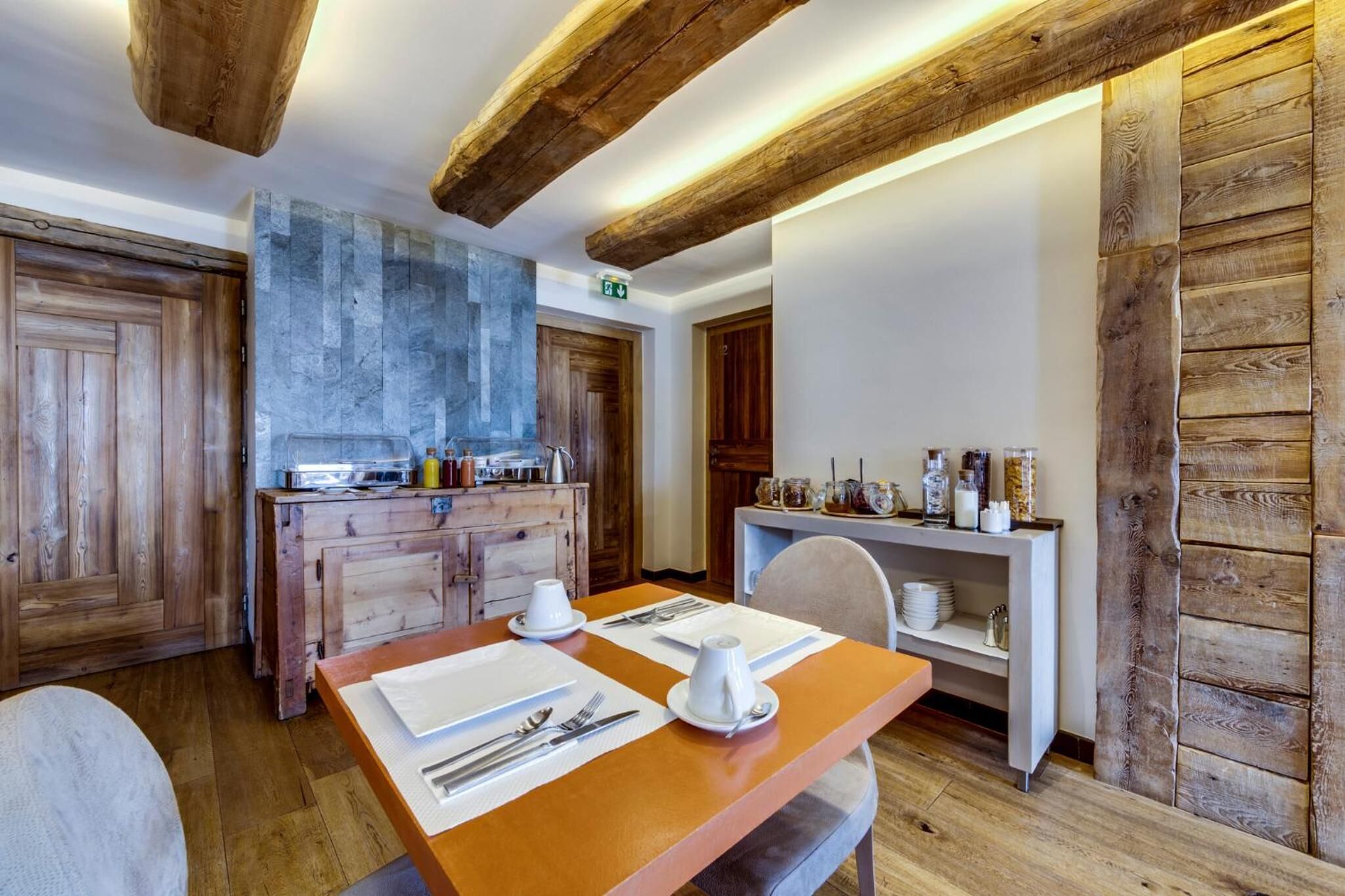 Une table de salle à manger en bois, mise avec de l’assiette blanche, des couverts en argent et un pichet blanc.