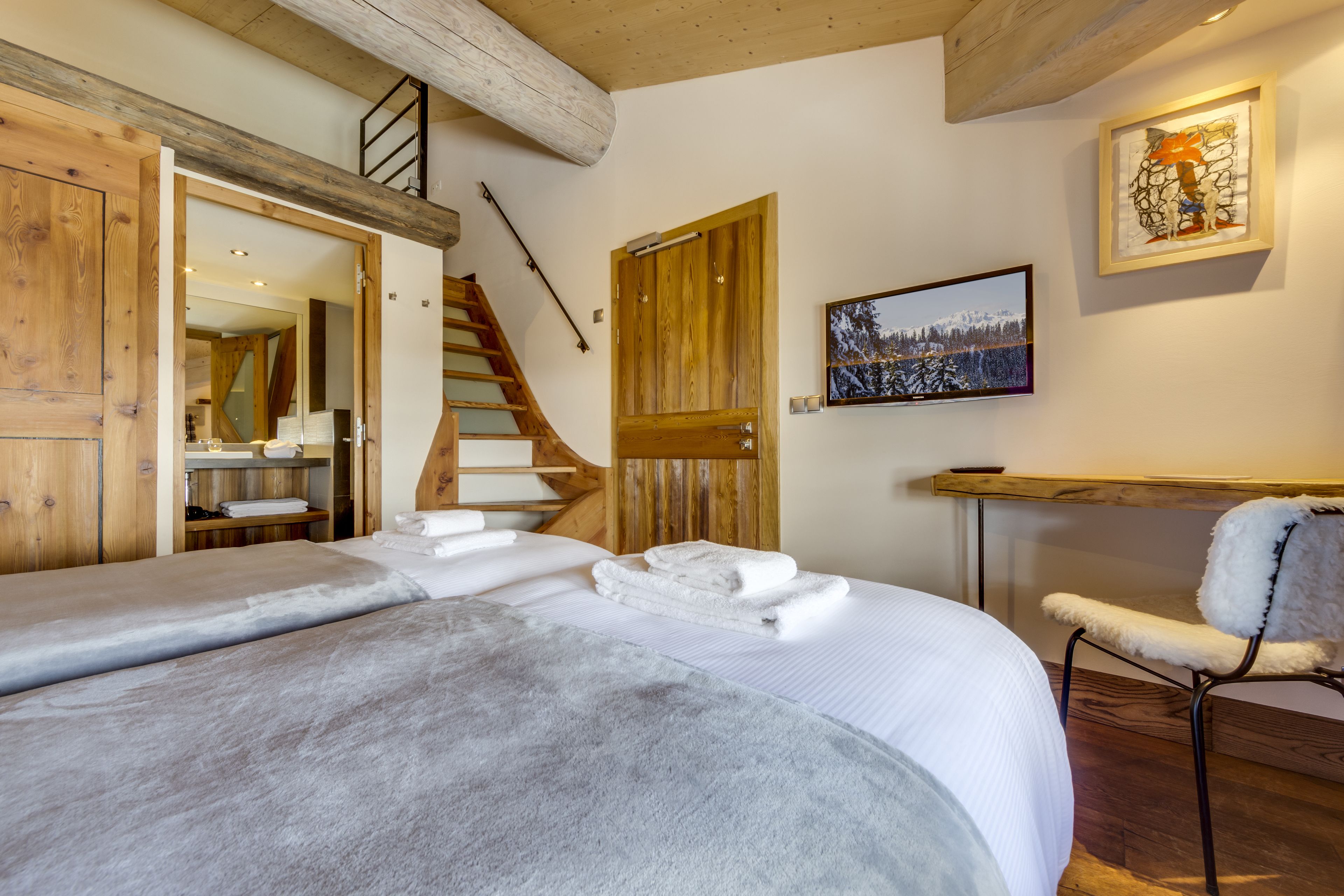 Een slaapkamer met twee bedden, houten deuren, een trap en een ingelijst schilderij aan de muur.