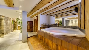 A modern spa area with a wooden deck, a hot tub, and a stone wall. - Chalet Hôtel du Fornet (Val-d'Isere)