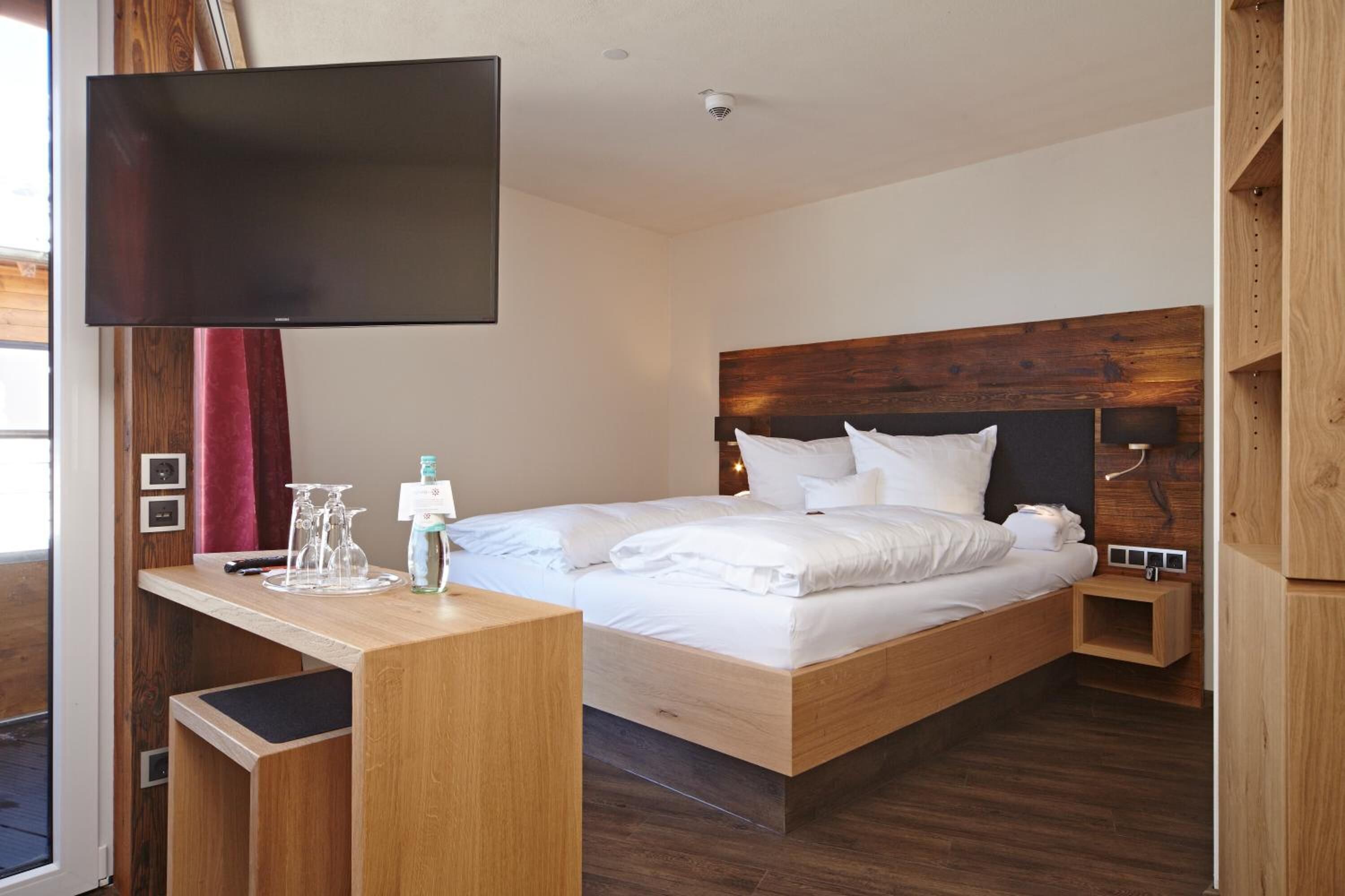 Een moderne hotelkamer met een houten bed, een flatscreen televisie, een nachtkastje met een lamp en een klein houten plankje.