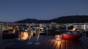 A table with two glasses of champagne, a candle, and a bowl of ice on a wooden deck overlooking a cityscape at dusk. - Shikikaboku (Kyoto)
