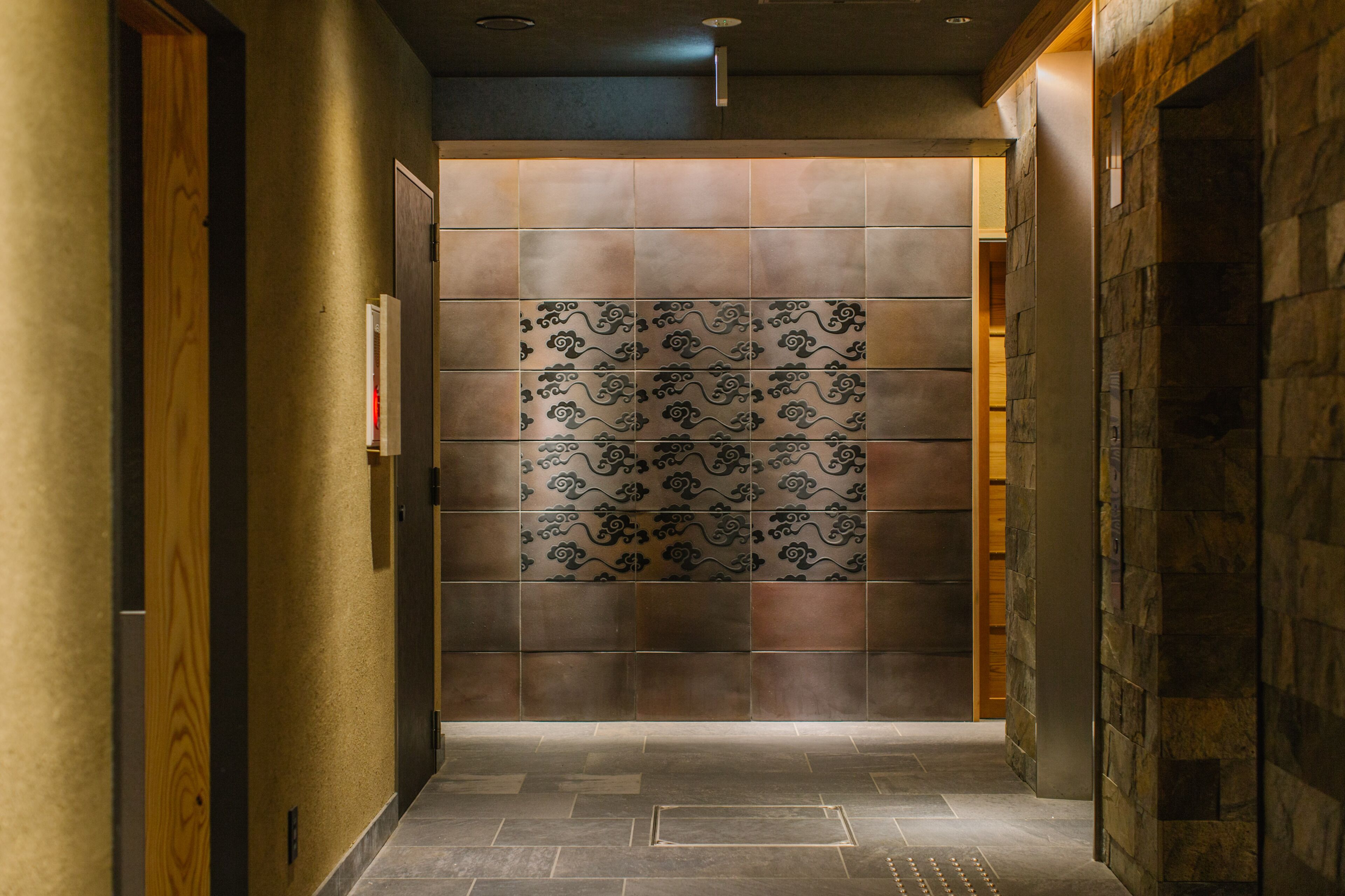 A hallway with a patterned wall, a wooden door frame, and a stone wall on the right.