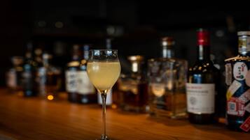 A bar with a glass of a light-colored beverage in the foreground, surrounded by various bottles and containers of alcohol.