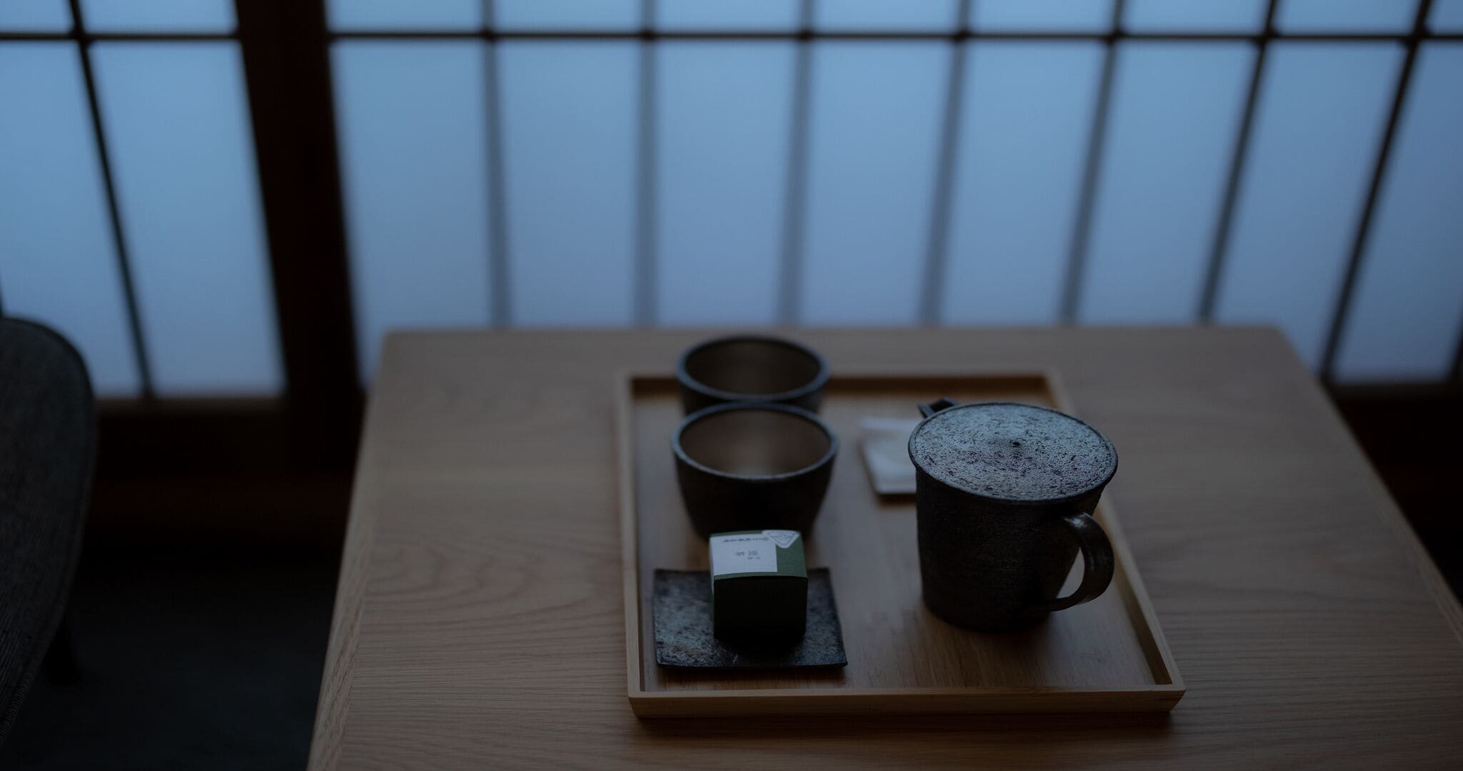 Taula de fusta amb una safata que conté tres tasses negres, una petita caixa i una mug negra.