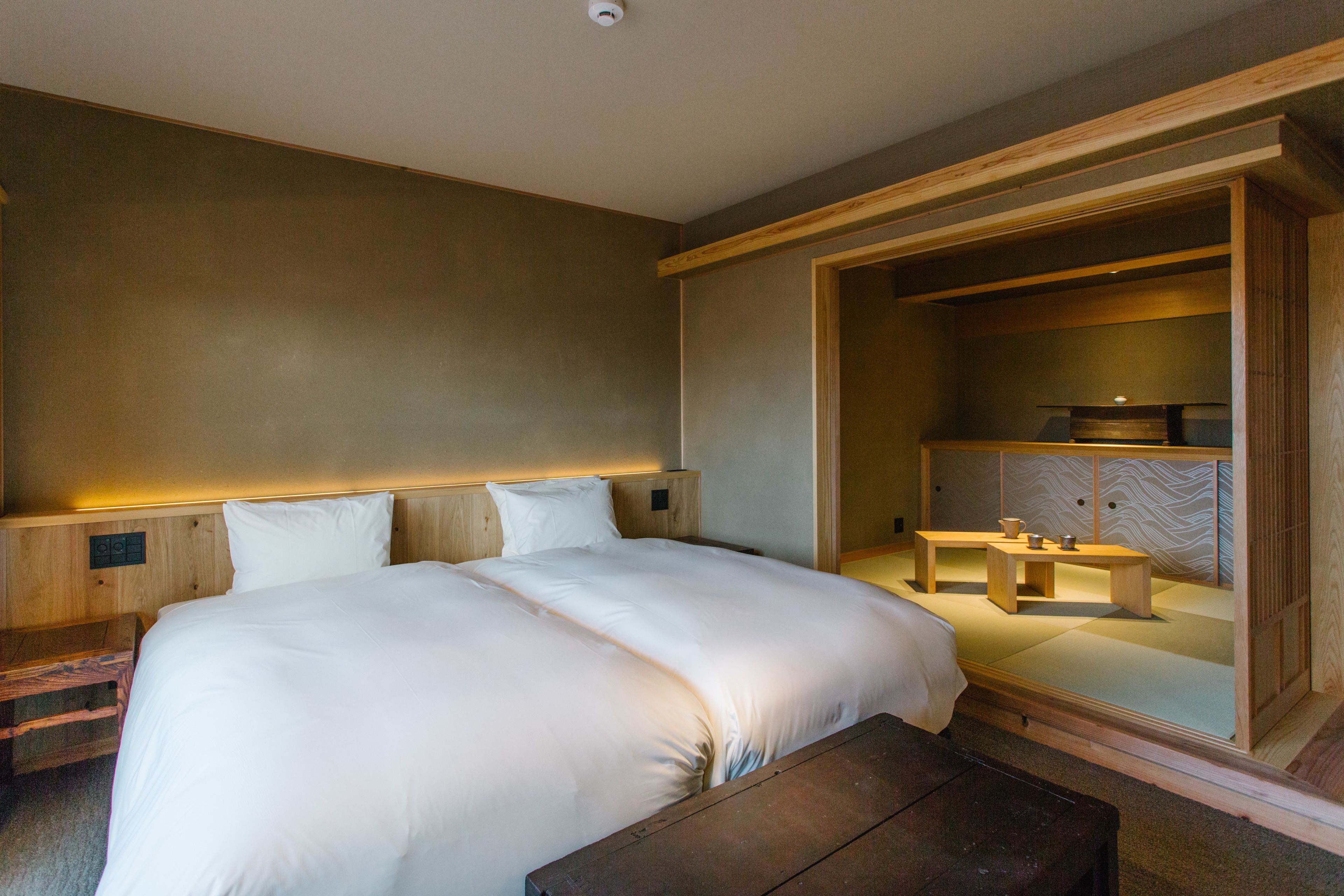Een moderne hotelkamer met een groot bed, een houten hoofdeinde en een zithoekje met een tafel en stoelen.