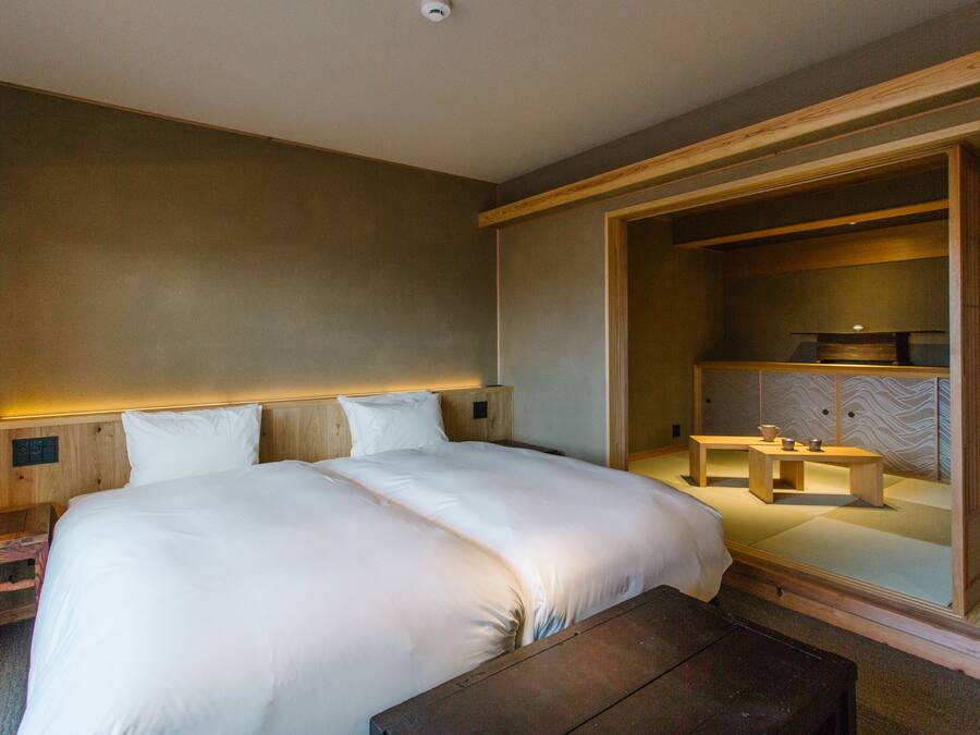 Een moderne hotelkamer met een groot bed, een houten hoofdeinde en een zithoekje met een tafel en stoelen.
