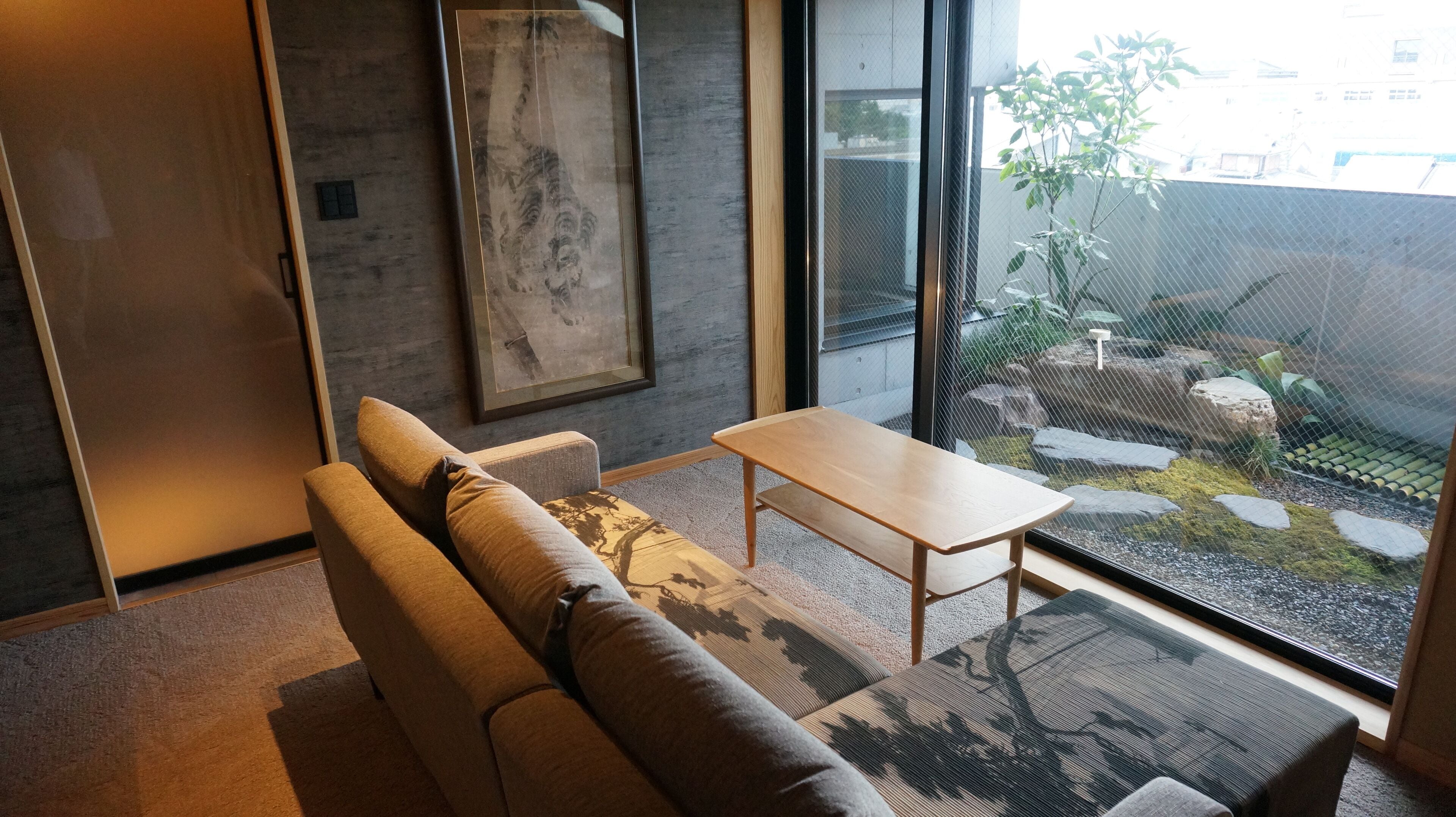 Uma sala de estar moderna com um sofá, uma mesinha e uma janela grande com vista para um jardim.