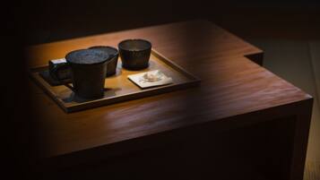A wooden table with a tray holding two dark ceramic cups and a small plate with a flower.