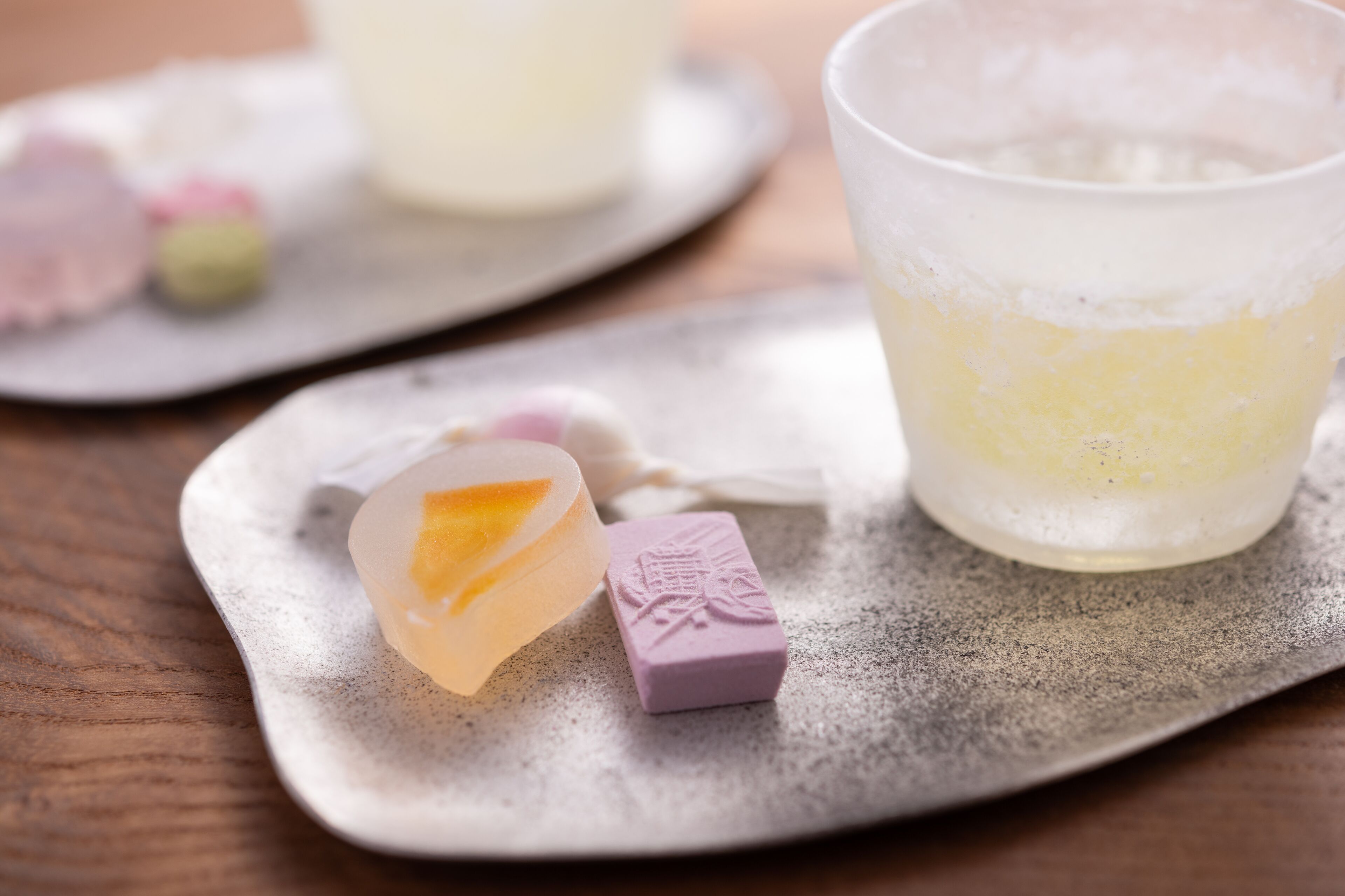 A table with a glass of a yellowish beverage, a small heart-shaped object, and a purple item with a design on it.