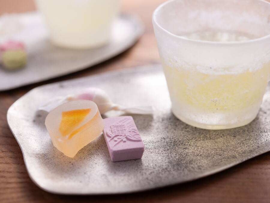 A table with a glass of a yellowish beverage, a small heart-shaped object, and a purple item with a design on it.