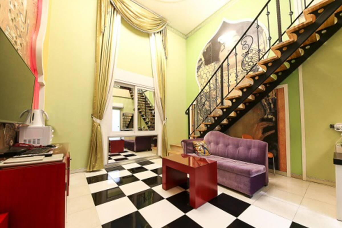 Un salon avec un sol à carreaux, un canapé violet, une table basse rouge et un escalier doté d’une rampe en métal.