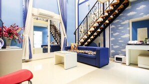 A modern living room with a blue sofa, white coffee table, and a red chair. A staircase with a black railing leads to an upper level. - Belita N Goodtime Drive-in Motel (Paju)