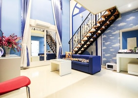 A modern living room with a blue sofa, white coffee table, and a red chair. A staircase with a black railing leads to an upper level.