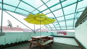 A covered outdoor area with a wooden table and benches, a yellow umbrella, and a satellite dish. - Belita N Goodtime Drive-in Motel (Paju)