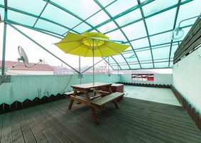 A covered outdoor area with a wooden table and benches, a yellow umbrella, and a satellite dish.