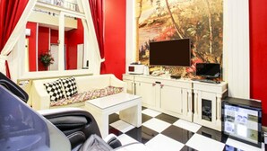A room with a checkered floor, a sofa with a patterned pillow, a TV on a stand, and a painting of a tropical scene. - Belita N Goodtime Drive-in Motel (Paju)