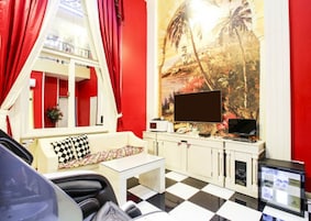 A room with a checkered floor, a sofa with a patterned pillow, a TV on a stand, and a painting of a tropical scene.