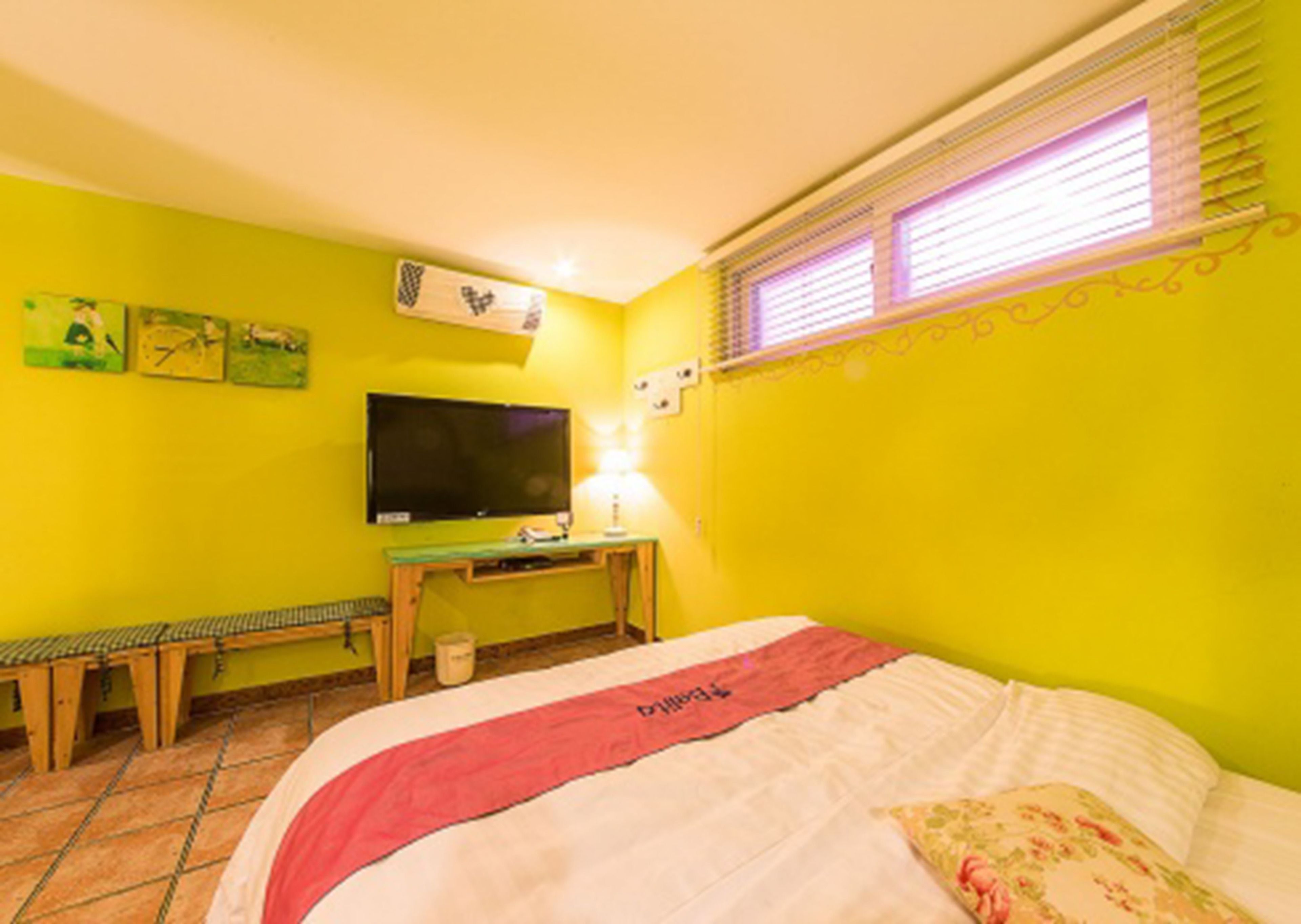 Ein Zimmer mit einem Bett, einem Schreibtisch mit Computer, einem Fernseher und Bildern an den Wänden.